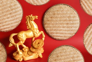 Gold-colored stone horse statue and bamboo tray on red background