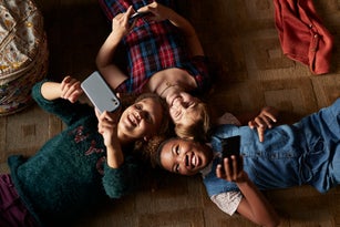 Top view of 3 tween girls laughing and looking at their smartphones