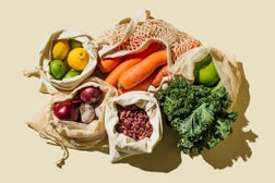 Variety Fresh of organic fruits and vegetables and healthy vegan meal ingredients in reusable eco cotton bags on beige background . Zero waste shopping concept. Healthy food, clean eating, eco friendly, no plastic. Flat lay, top view