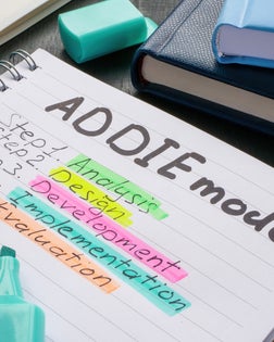 Desk with notepads and one with ADDIE model marks.