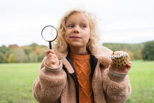 Curious girl with muffin and magnifying glass in nature