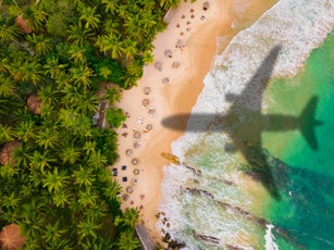 Airplane silhouette over a tropical beach with palm trees. Travel and resort vacation concept