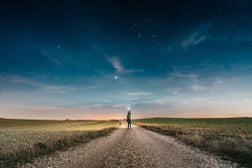 Woman pointing a lantern to the sky while walking on a country road at night with the clear sky full of stars