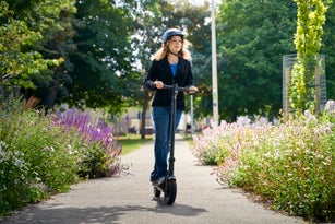 Young woman smiling riding an E scooter through the city paths