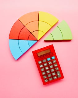 High angle view of a pie chart made of colorful building blocks and red calculator on pink background