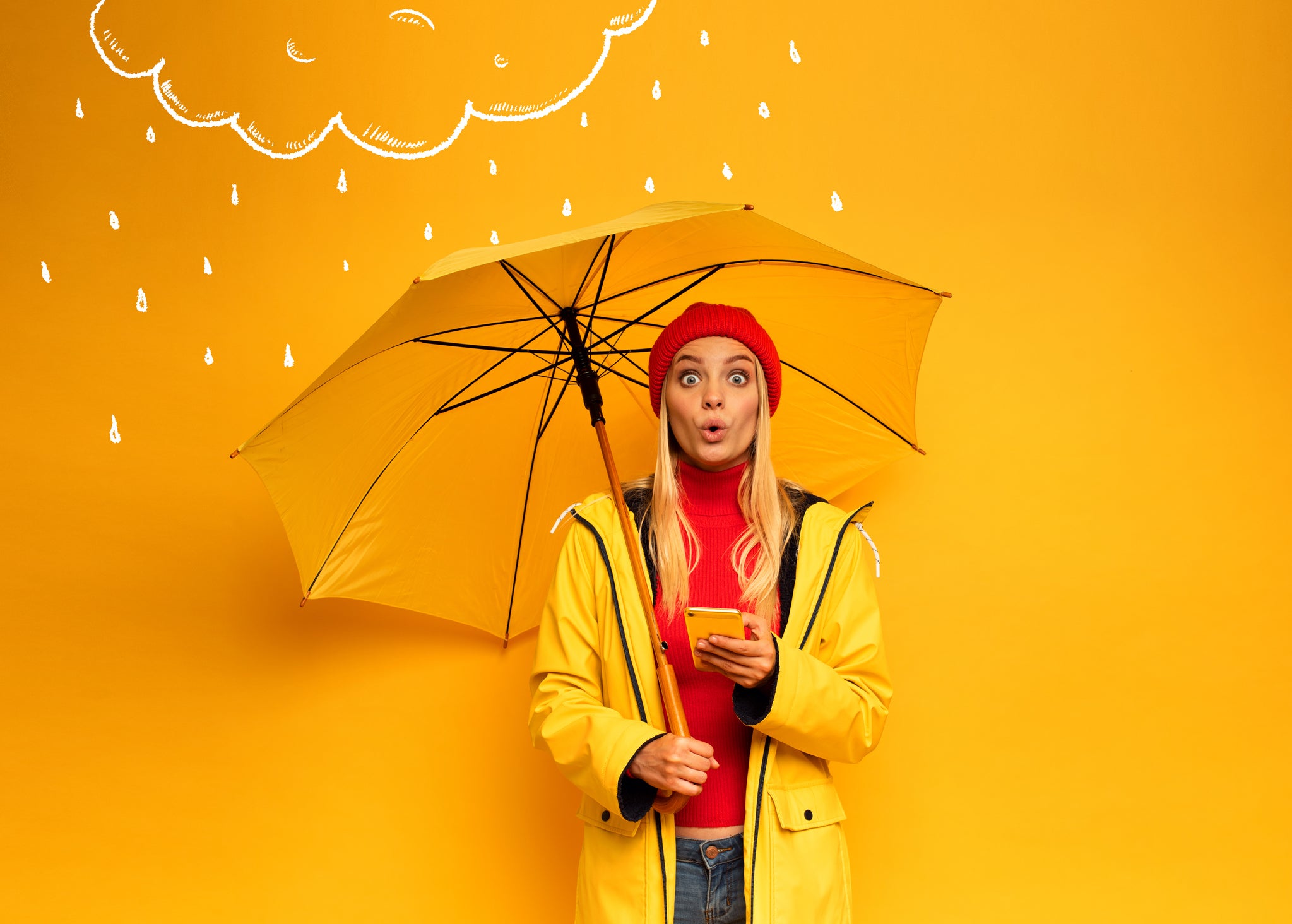 Girl with smartphone and umbrella on yellow background surprised for the weather