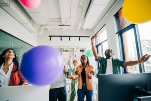 A joyful team plays with colorful balloons in a bright modern office. The vibrant scene conveys fun, creativity, and positive workplace energy.