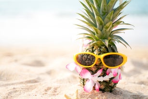Summer in the party.  Hipster Pineapple Fashion in sunglass and listen music with sunblock and sandal on the sand beach beautiful blue sky background.