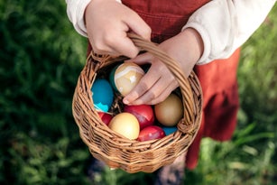 Little girl hands holding multicolored Easter eggs in the basket outdoors.