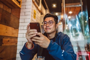 Young handsome Asian man making order from the digital menu on smartphone in restaurant