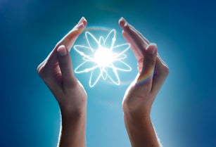 Hands cupping a glowing atom in the studio
