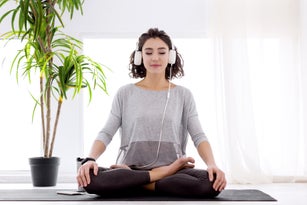 Modern woman with headphones sitting in yoga lotus posture