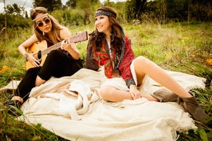 Hippy girls on blanket in field, playing guitar
