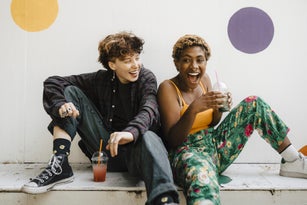 Cheerful friends sitting with drinks on retaining wall
