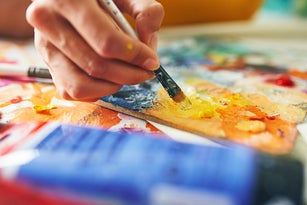 Artist's hand masterfully blending colors on a palette. Vivid yellow and blue hues dominate in this close-up artistry scene.