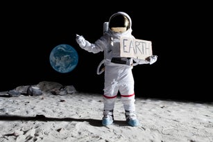 A creative image of an astronaut, on the moon,  holding an 'EARTH' sign.