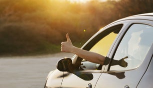Man showing thumbs up from car window at sunset