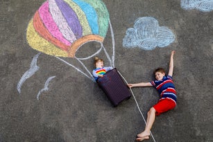Happy little toddler girl and kid boy flying in hot air balloon painted with colorful chalks in rainbow colors on ground or asphalt in summer. Two children, siblings having fun. Creative leisure
