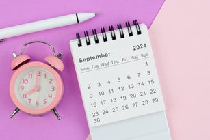 Desk Calendar 2024: September calendar is used to plan daily work and life with white pen and alarm clock against a two-tone background.