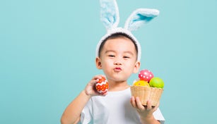 Asian cute little child boy smile beaming wearing bunny ears and a white T-shirt, standing to hold a basket with full Easter eggs. And other hand holds an easter egg