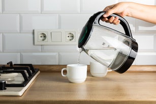 A man makes tea using boiling water from an electric kettle in the kitchen at home. It's time to have breakfast and drink tea. Modern electric kettle on a wooden table. Kettle for boiling water.