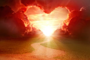 Red heart shaped sky at sunset. Beautiful landscape with flowers.Love background with copy space. Road to love