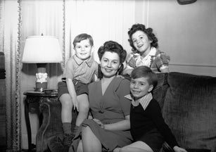 Mother with three children (4-5, 6-7, 8-9) posing in living room, (B&W), portrait