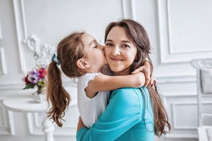 little girl about 10 years old embracing and kissing her smiling beautiful mother both looking at camera, family