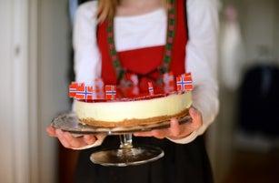 girl dressed in national clothes holding a cheesecake decorated with norwegian flags